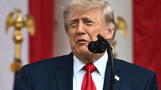 Donald Trump spricht vor einem rot-weiß gestreiften Hintergrund in ein Mikrofon.