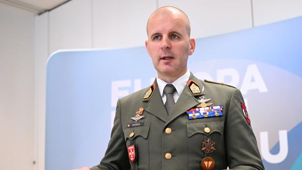 Markus Reisner spricht gestikulierend vor einem farbigen Hintergrund mit Schriftzug.