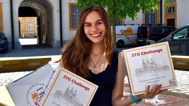 Junge Frau mit langen Haaren hält draußen mehrere Spielekartons mit der Aufschrift „STG Challenge“ und lächelt.