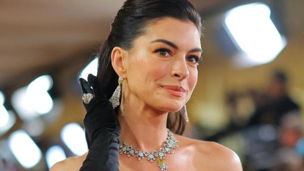Anne Hathaway mit hochgesteckten Haaren, Diamantschmuck und schwarzen Handschuhen.