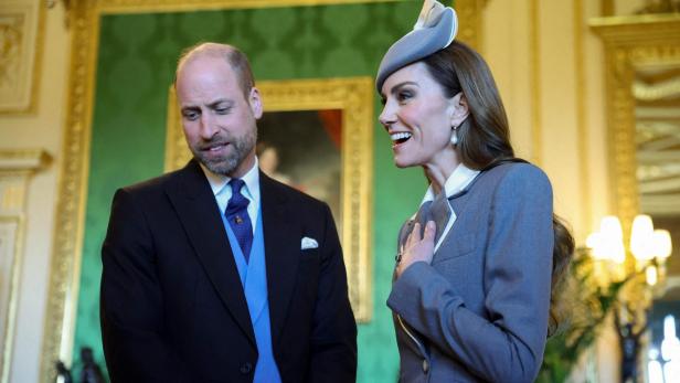 Prinz William und Prinzessin Kate in formeller Kleidung, sie lächelt mit der Hand auf der Brust.