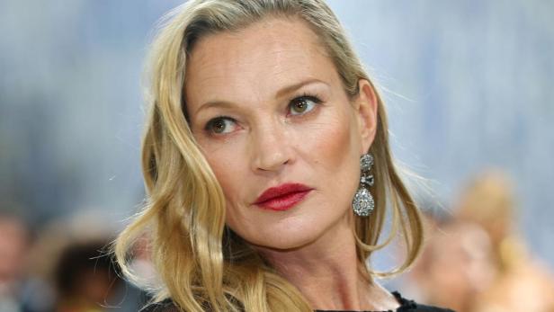 Kate Moss trägt ein transparentes, schwarzes Kleid und auffällige Ohrringe.