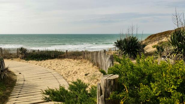 Sandstrand mit Holzsteg und Dünenvegetation an der Atlantikküste bei Lège-Cap-Ferret im Département Gironde, wo aktuell gefährliche Strömungen herrschen.