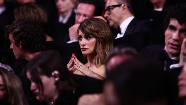 Penélope Cruz sitzt im Publikum, die Hände gefaltet, umgeben von anderen Gästen.
