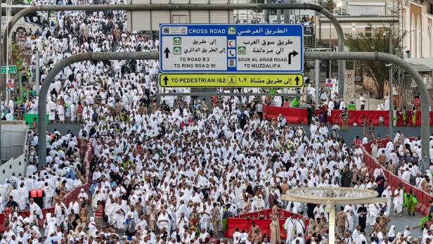 Eine große Menschenmenge in weißer Kleidung bewegt sich unter einem Wegweiser in Mekka.