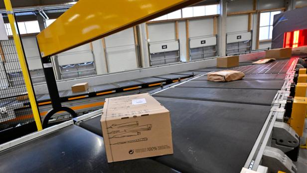 Pakete und Päckchen werden auf einem Förderband in einer modernen Lagerhalle transportiert.