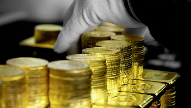 Gestapelte Goldmünzen und Goldbarren werden von einer Hand mit weißem Handschuh sortiert.