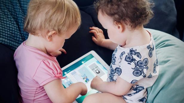 zwei Kleinkinder sitzen auf dem Sofa, während sie einen Tablet-Computer benutzen