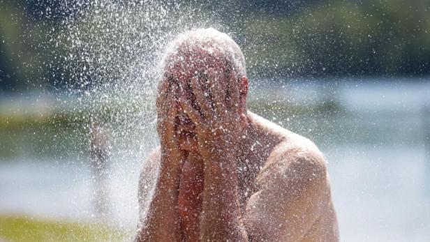 Ein Mann bedeckt im Freien sein Gesicht mit den Händen, während Wasser auf ihn herabprasselt.