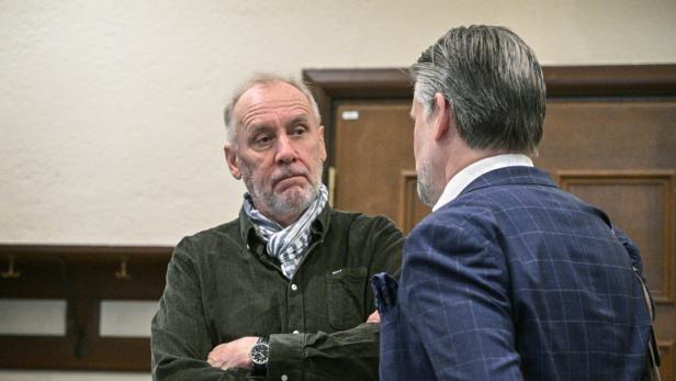 Håkan Nesser und sein Anwalt unterhalten sich, Nesser mit verschränkten Armen und Schal, der andere Mann im karierten Sakko.