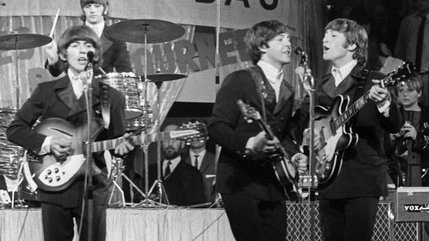 Die Beatles spielen auf einer Bühne vor Mikrofonen und Schlagzeug.