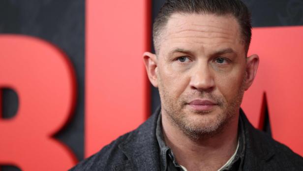 Tom Hardy blickt vor einem roten Hintergrund zur Seite.