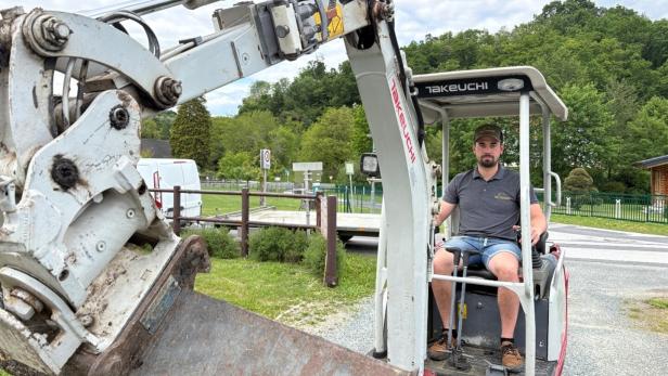 Ein Mann sitzt in einem kleinen Takeuchi-Bagger vor einer grünen Landschaft.