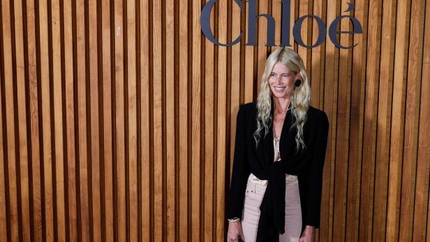 Claudia Schiffer lächelt vor einer Holzwand mit dem Chloé-Logo.