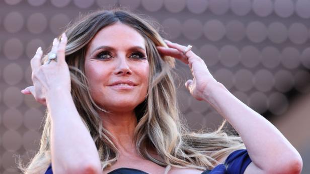 Heidi Klum posiert in einem blauen Kleid und mit auffälligen Ringen im Haar.