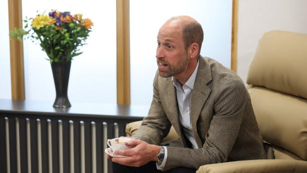 William im Sessel hält eine Teetasse in der Hand, neben ihm steht eine Blumenvase.