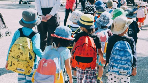 Mehrere Kindergartenkinder mit bunten Rucksäcken gehen in einer Gruppe im Freien.