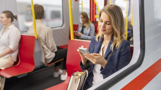 Frau in Businesskleidung sitzt in einer U-Bahn und nutzt ihr Smartphone.