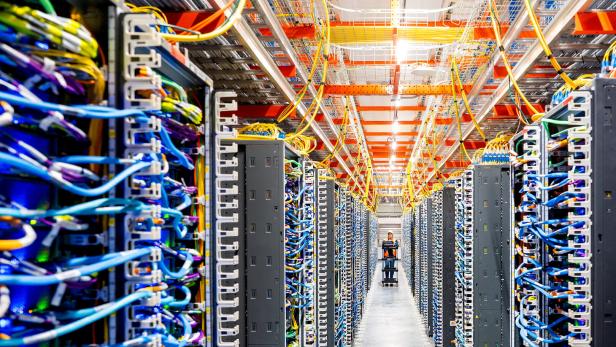 Reihen von Serverracks mit bunten Kabeln und einer Person, die einen Wagen durch einen Gang schiebt.
