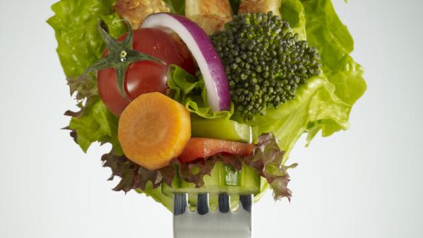 Verschiedene Gemüsestücke, Salat und Hähnchenstreifen sind auf einer Gabel aufgespießt.