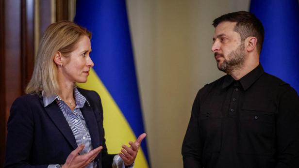 Eine Frau und ein Mann stehen sich gegenüber und sprechen, im Hintergrund sind ukrainische Flaggen zu sehen.