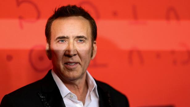 Nicolas Cage vor rotem Hintergrund mit undeutlichen Schriftzeichen.