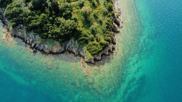 Luftaufnahme einer bewaldeten Inselküste mit klarem, türkisfarbenem Wasser im Ionischen Meer.
