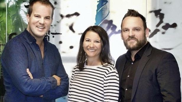 Drei Personen posieren vor einem abstrakten Kunstwerk.