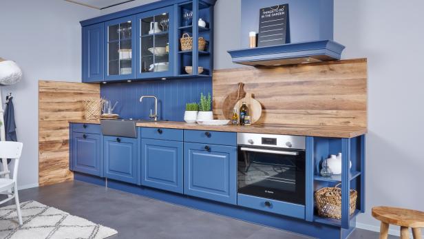 Moderne Küche mit blauen Schränken, Holzarbeitsplatte, Einbauofen, Spüle, Deko und Kräutertöpfen.