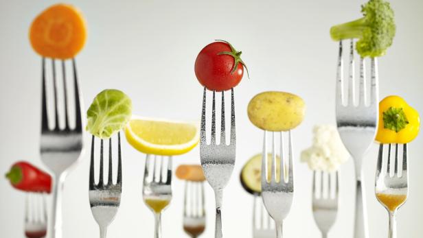 Mehrere Gabeln halten verschiedene Gemüsestücke wie Tomate, Brokkoli, Karotte, Paprika und Kartoffel.