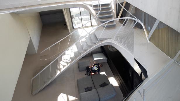 Moderne, helle Innenarchitektur mit geschwungener Treppe, grauen Sofas und einer Person, die auf dem Boden sitzt.