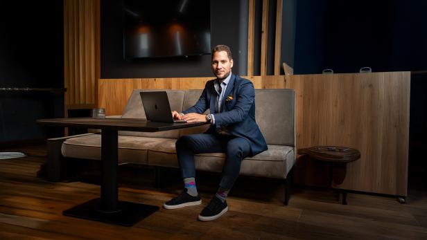 Ein Mann im Anzug sitzt an einem Tisch mit einem Laptop in einem modern eingerichteten Raum.