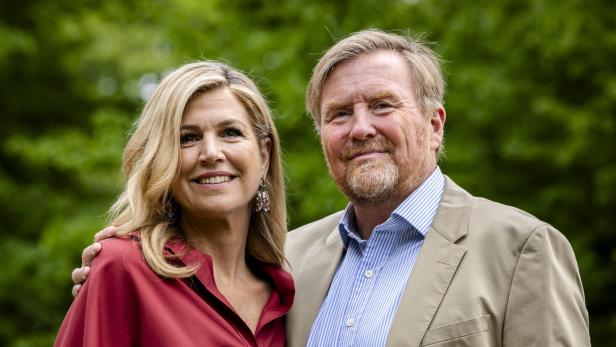 König Willem-Alexander und Königin Máxima lächeln vor grünem Hintergrund.