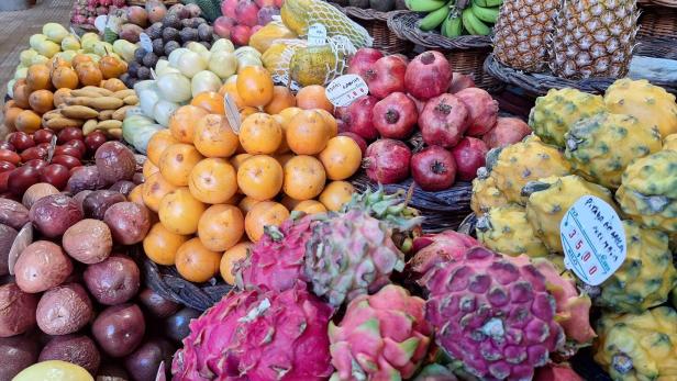 Auf einem Marktstand türmen sich exotische Früchte wie Drachenfrucht, Ananas, Bananen und Orangen.