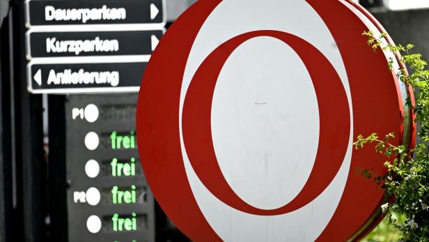 Ein rotes, rundes Logo mit weißem O steht neben einer Parkplatzanzeige mit der grünen Aufschrift „frei“ und Wegweisern für Gäste und Parkbereiche.