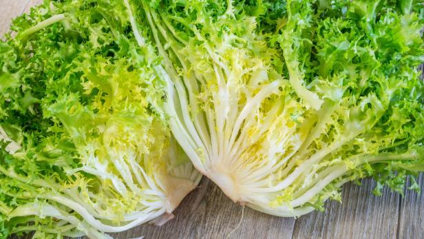 Aufgeschnittener Endiviensalat mit krausen, grünen und gelben Blättern auf einer Holzoberfläche.