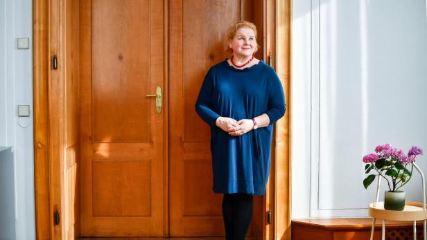 Eine Frau im blauen Kleid, es ist Sozialministerin Schumann, steht vor einer braunen Tür