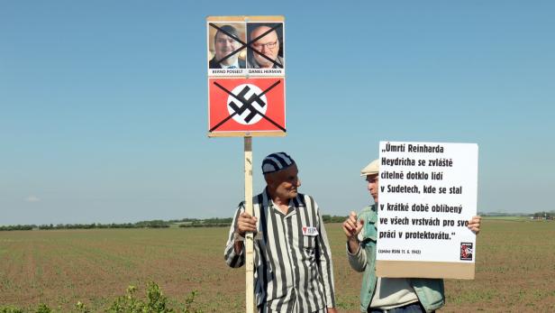 Ein Mann verkleidet als KZ-Häftling hält ein Plakat mit durchgestrichenem Hakenkreuz hoch.