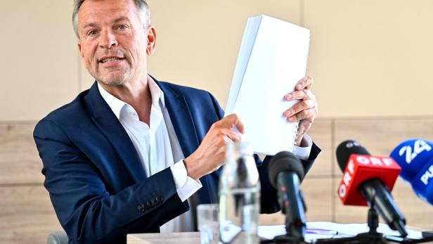 Ein Mann im Anzug präsentiert Dokumente vor Mikrofonen von ORF und anderen Sendern.
