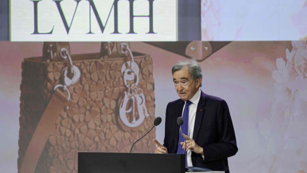 Bernard Arnault spricht vor einem LVMH-Logo, im Hintergrund eine Handtasche.