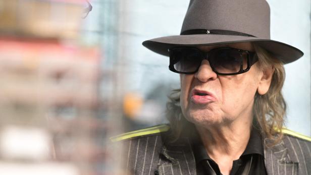 Udo Lindenberg mit Hut und Sonnenbrille, im gestreiften Anzug, spricht.