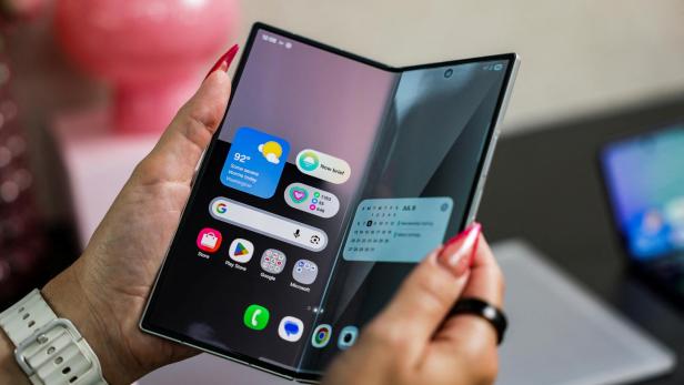Eine Person hält ein faltbares Smartphone mit Wetter- und Kalender-Widgets in der Hand.