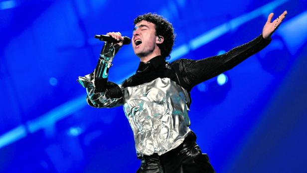 Eine Person mit silberner Rüstung und Mikrofon singt leidenschaftlich auf einer Bühne mit blauem Licht.