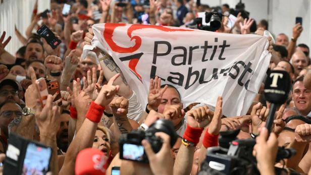 Menschenmenge jubelt und hält ein Transparent mit der Aufschrift „Partit Laburista“ sowie zahlreiche Kameras und Mikrofone.