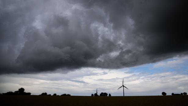 Dunkle Gewitterwolken ziehen über eine Landschaft mit Windrädern und vereinzelten Bäumen am Horizont.