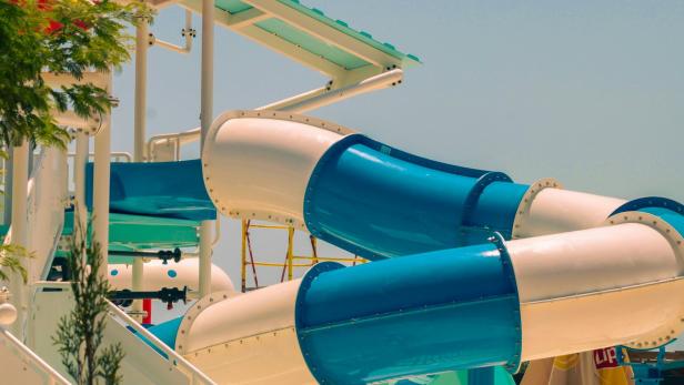 Verschlungene blaue und weiße Wasserrutsche in einem Freizeitbad bei sonnigem Wetter.