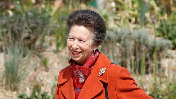 Eine lächelnde Prinzessin Anne trägt einen orangefarbenen Mantel und einen roten Schal im Freien.