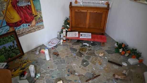 Ein kleiner Andachtsraum mit umgestürzten Kerzen, zerbrochenen Gegenständen und verstreuten Papieren auf dem Boden.