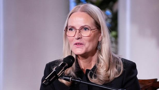 Mette-Marit mit Brille spricht in ein Mikrofon.