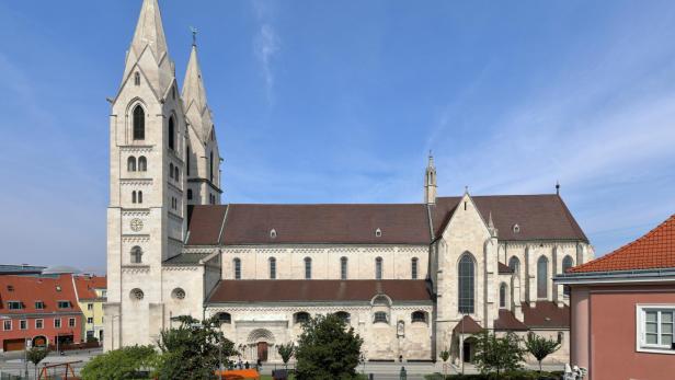 Große Kirche mit zwei hohen Türmen, rotem Dach und Spielplatz im Vordergrund an einem sonnigen Tag.